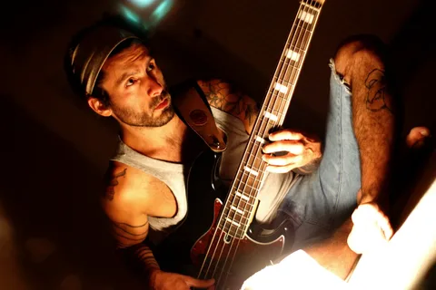 Shoeless man in jean shorts playing bass guitar