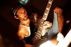 Shoeless man in jean shorts playing bass guitar